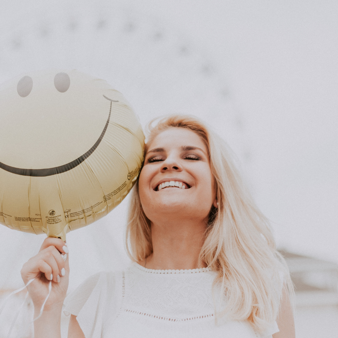 femme qui sourit tenatn un ballon jaune qui a un sourire dessiné